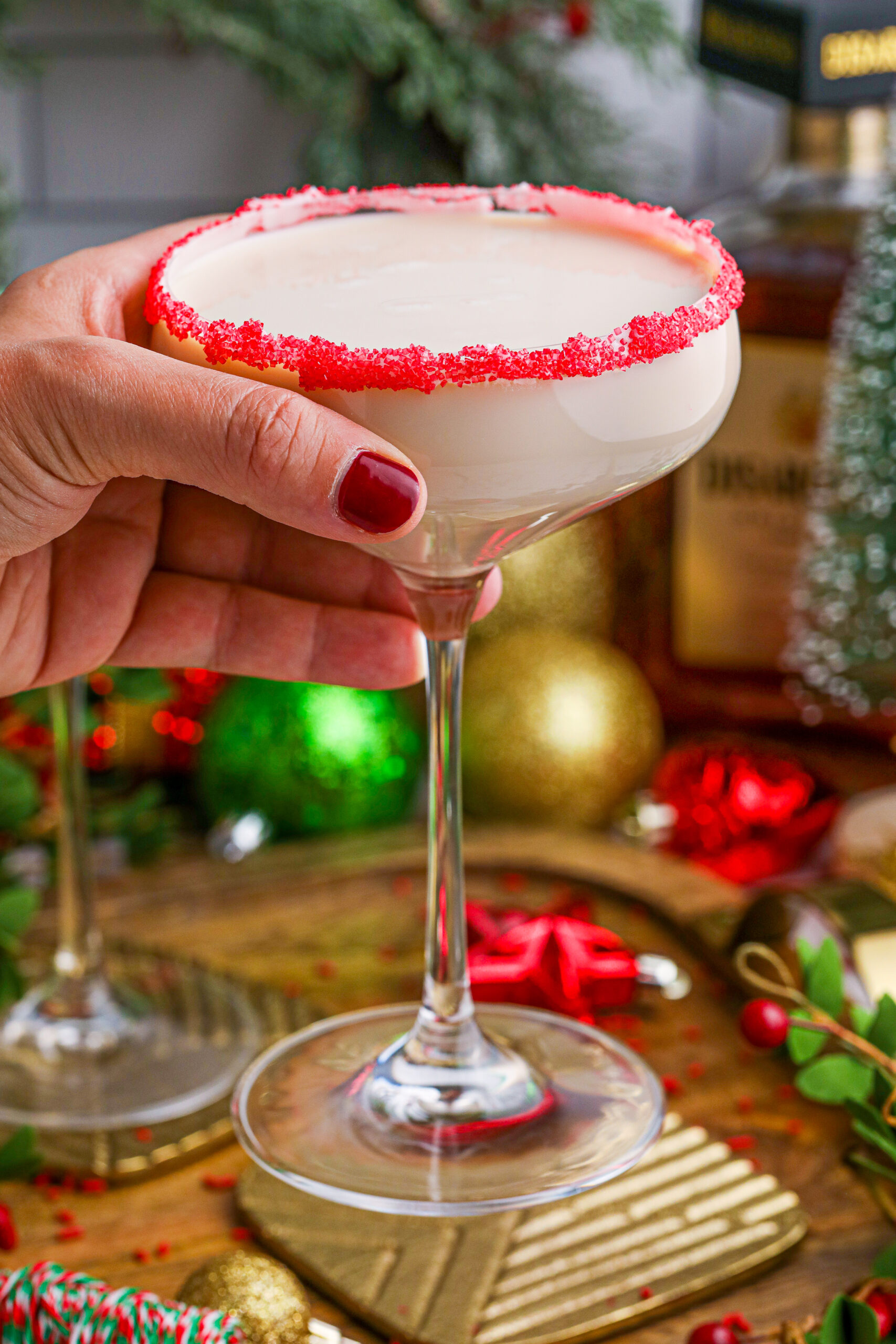 Sugar Cookie Cocktails in a glass with a red sugar rim being held by a hand