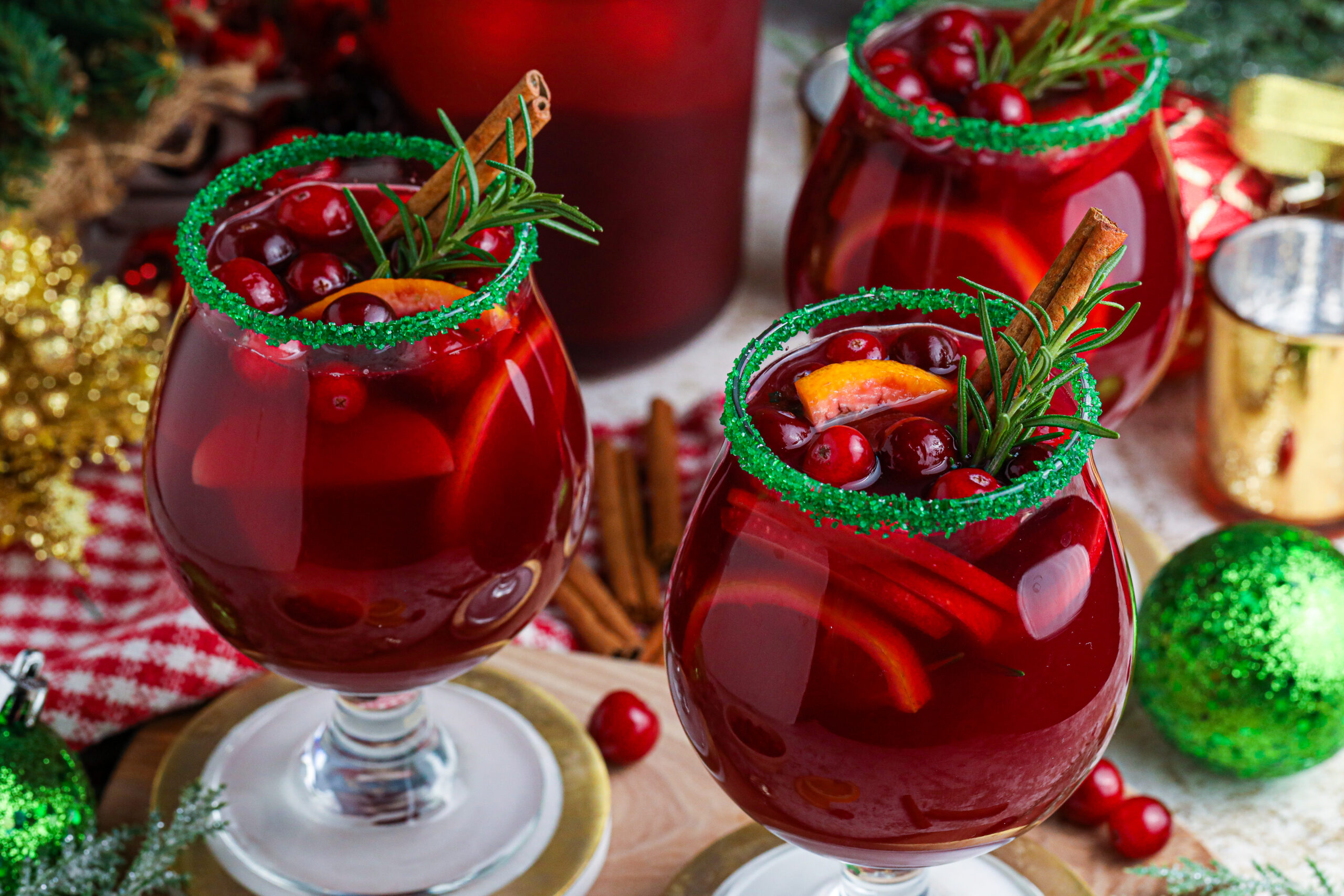 red christmas sangria in glasses with a green sugar rim on a wood table