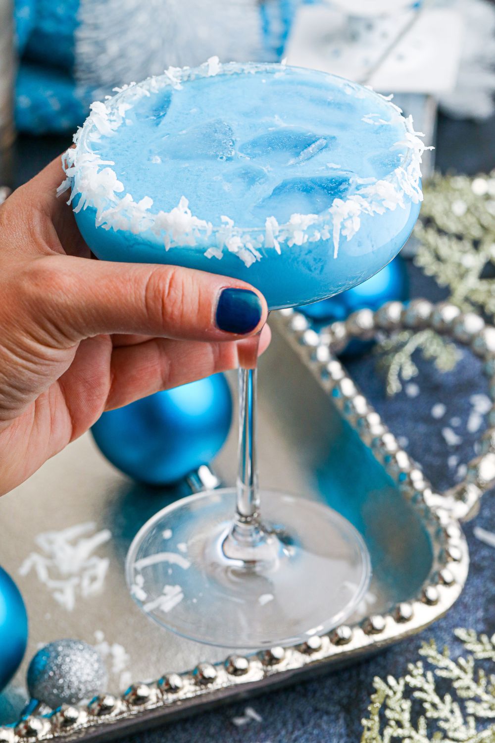 woman holding cocktail glass with blue drink in hand 
