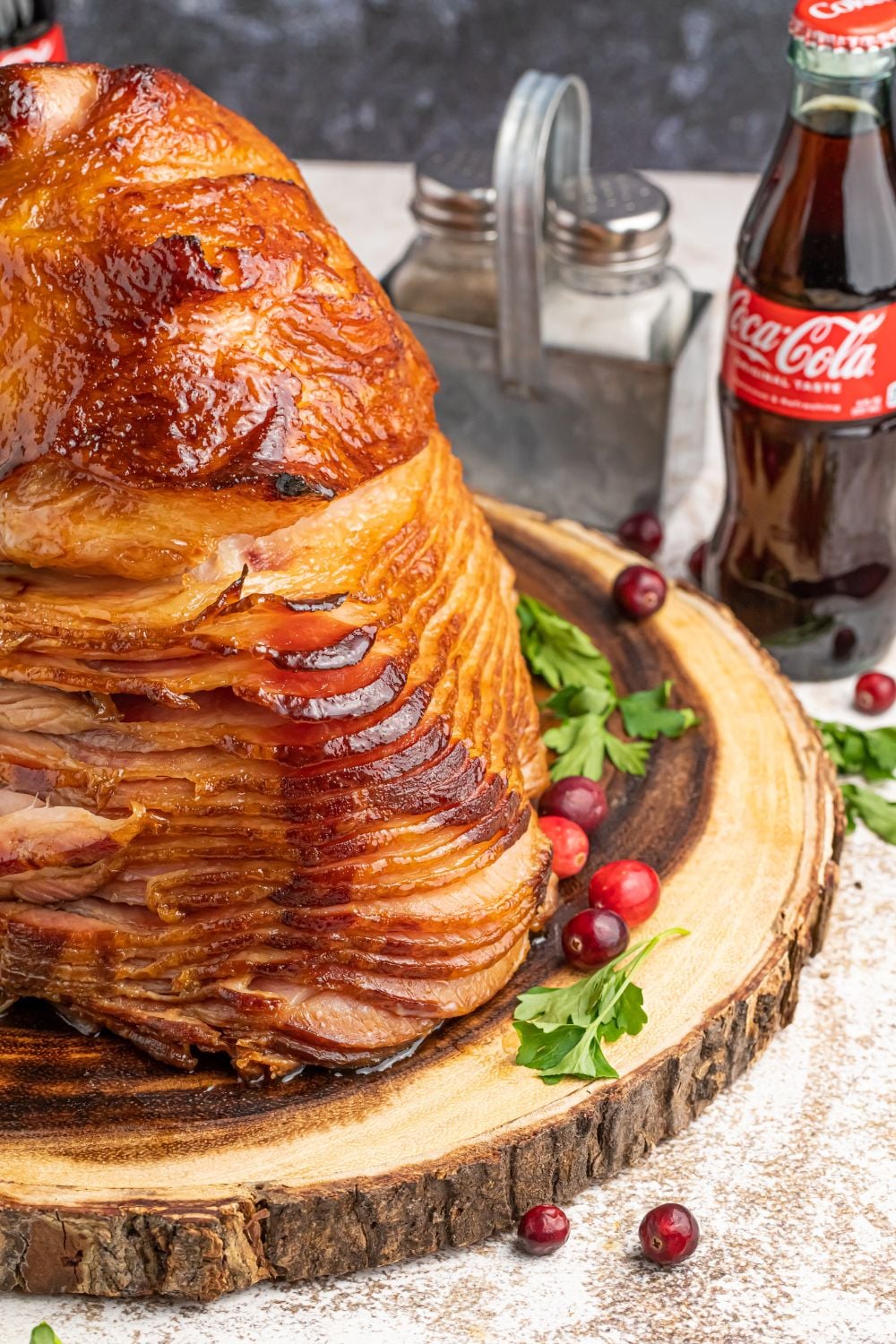spiral ham on wooden platter with salt and pepper behind it and coke
