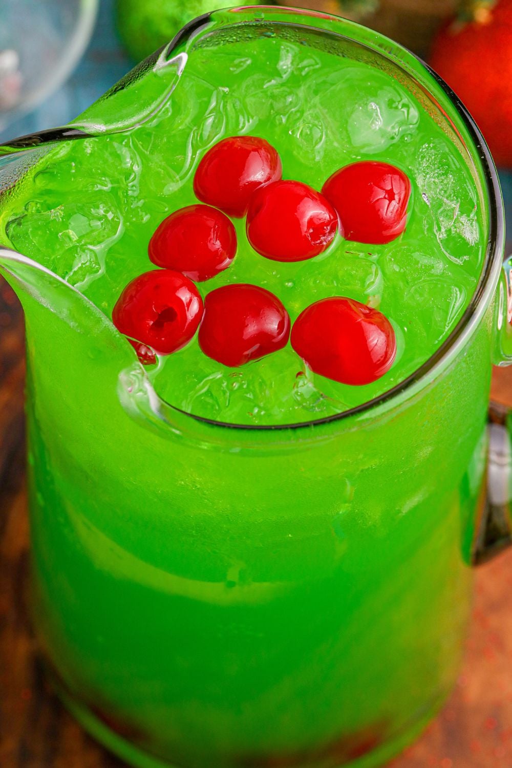 punch in a pitcher with red cherries on top of the green punch in container