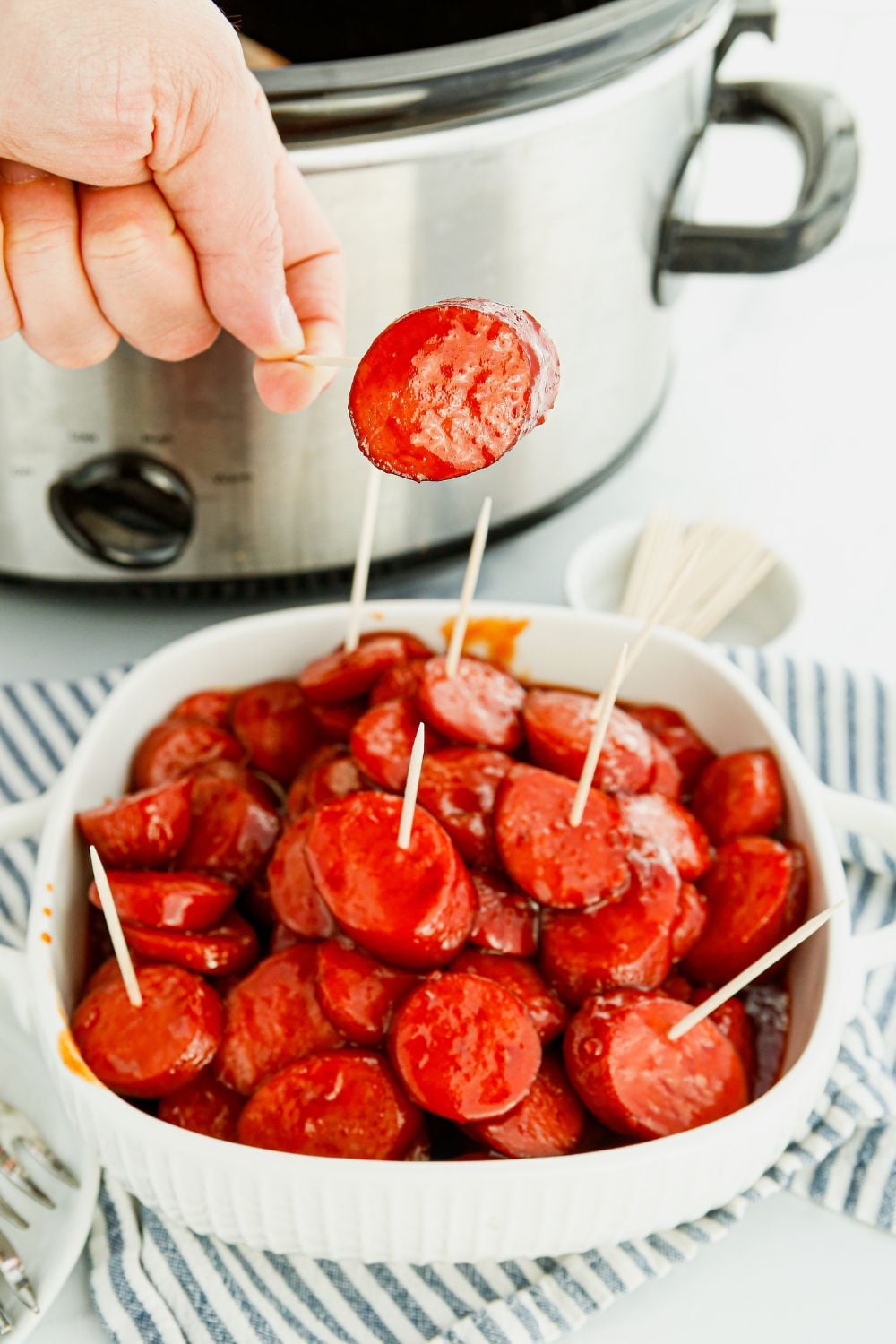 person holding toothpick with kielbasa on it