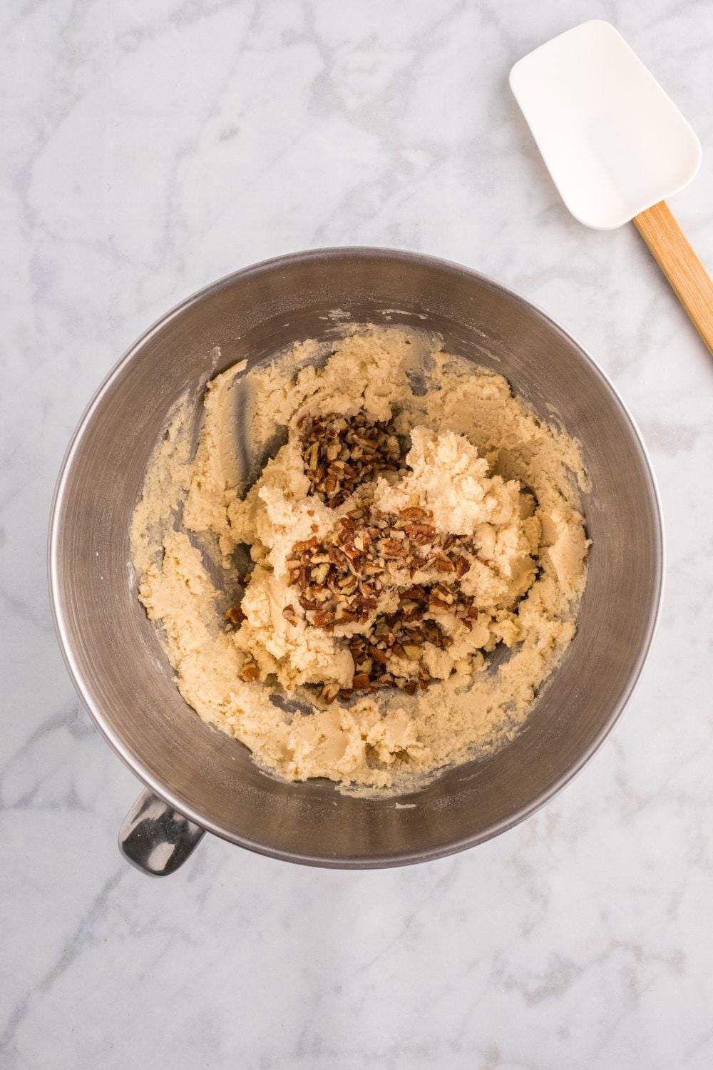 cookie dough in a mixing bowl with chopped nuts poured in bowl