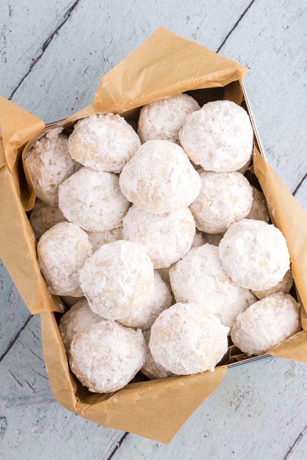 container of snowball cookies sitting on wooden table