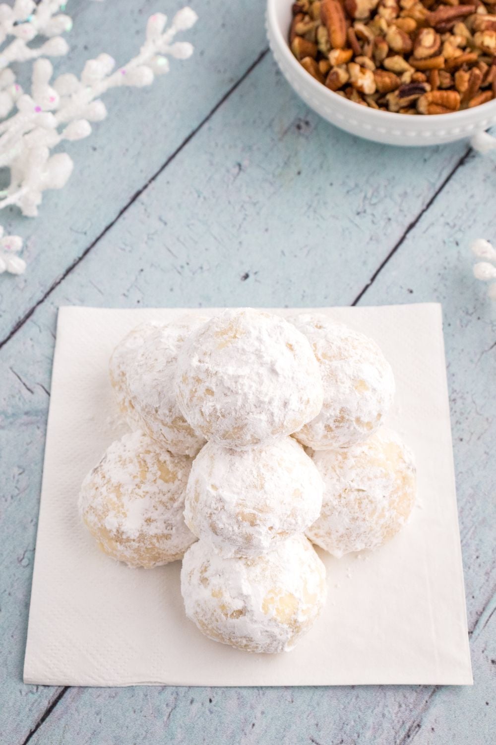snowball cookies on a plate on table with bowl of nuts behind it