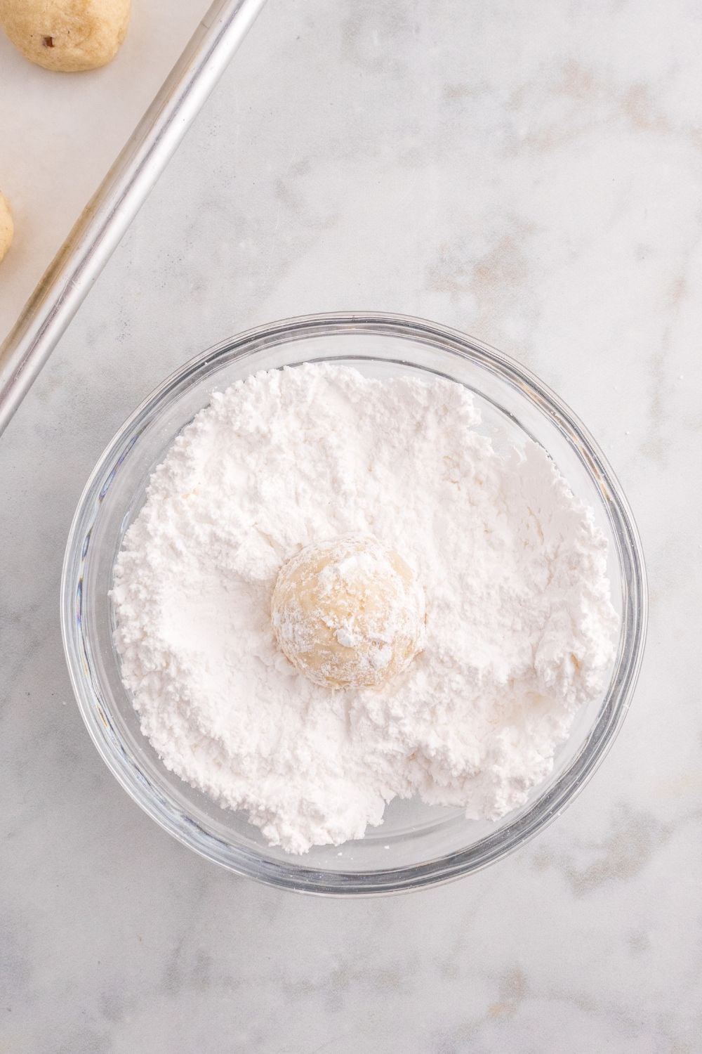 cookie being rolled in a bowl with powdered sugar
