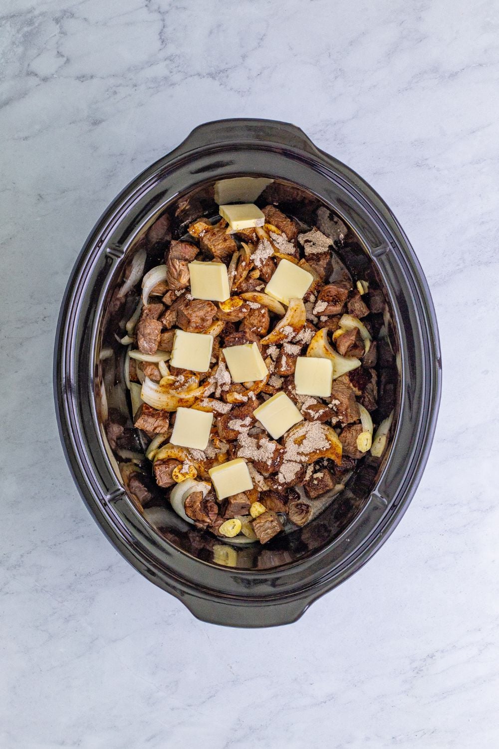 steak bites and mixture in a crockpot with slices of butter on top