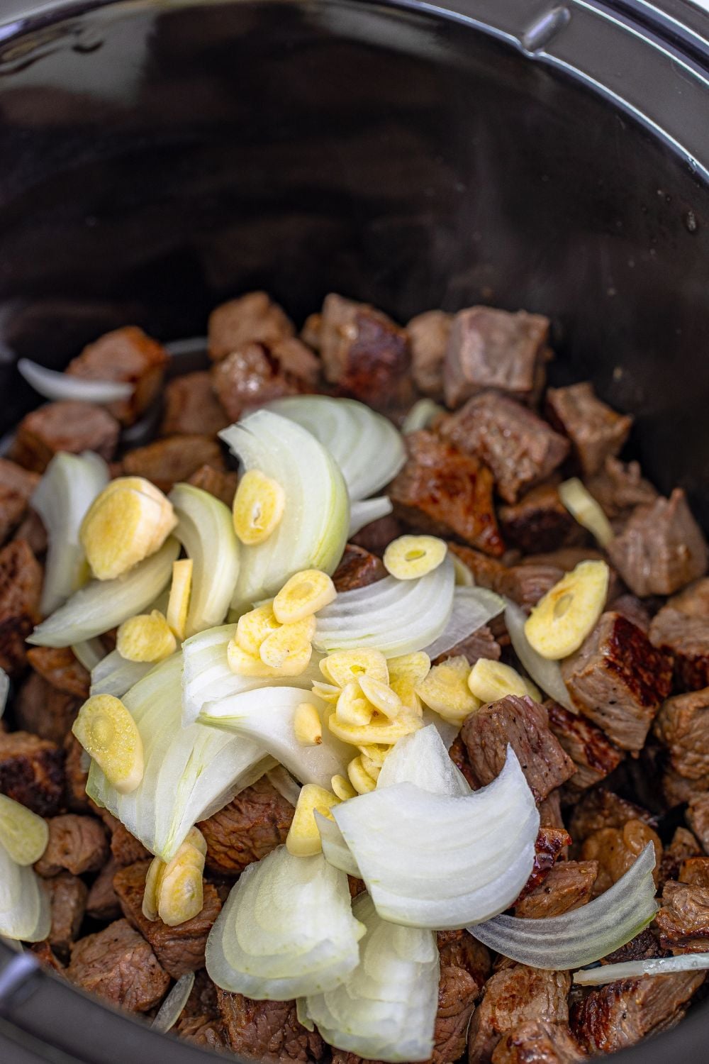 garlic and onions on top of seared steak in a crockpot