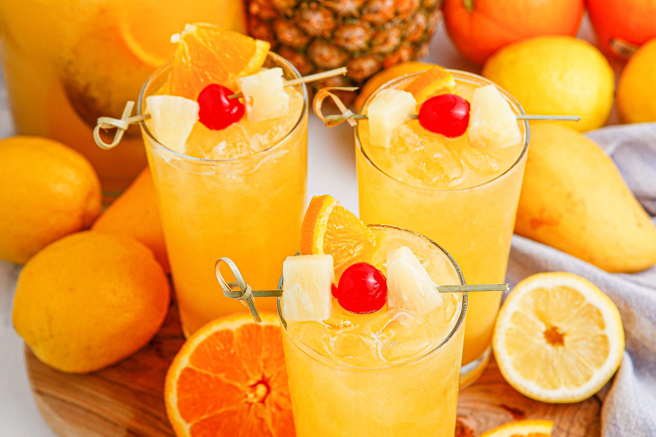 overhead shot of Tropical Lemonade Punch in 3 tall clear glasses on a wooden table with fruit around it