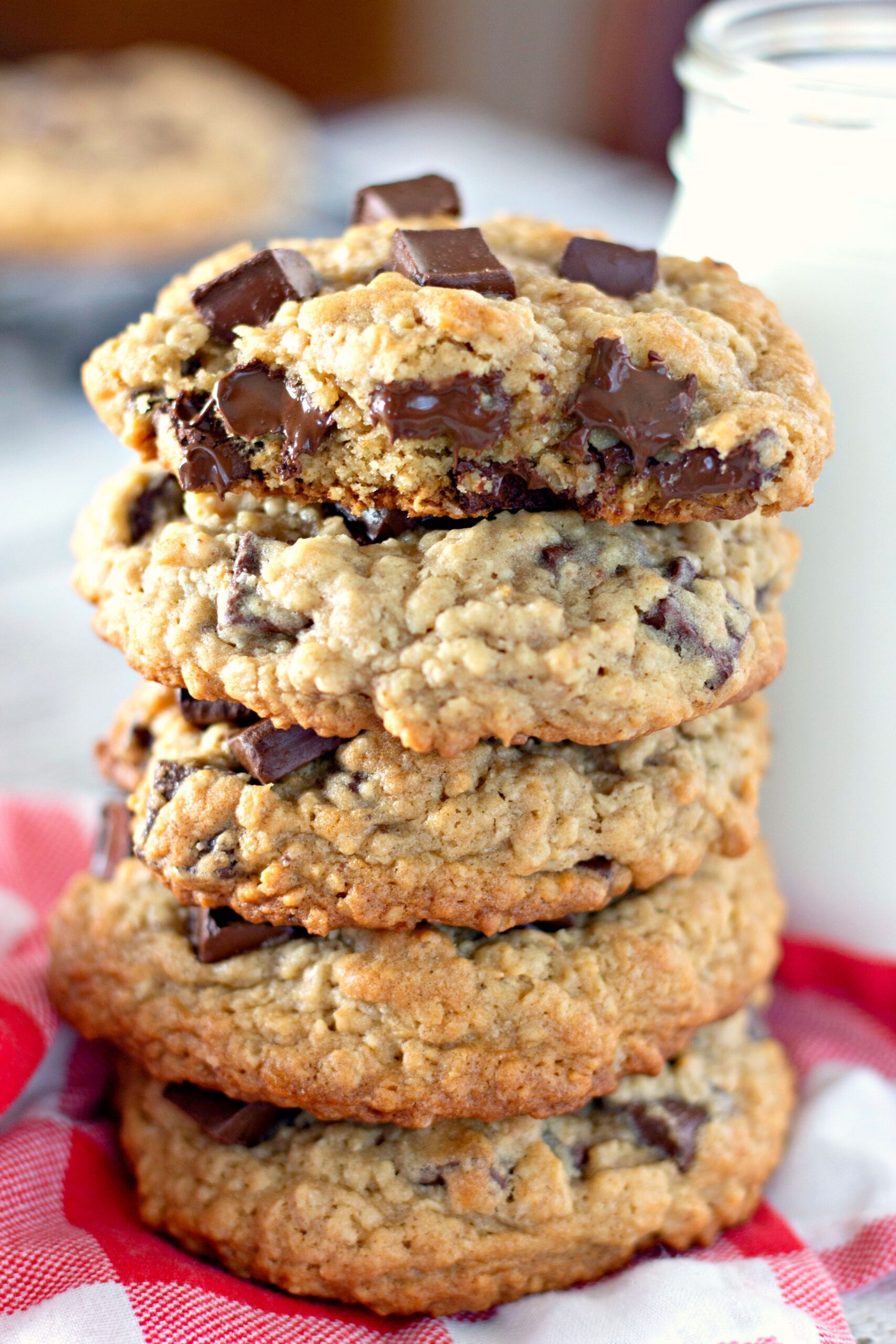 stacked chocolate chunk cookies on table with glass of milk on side
