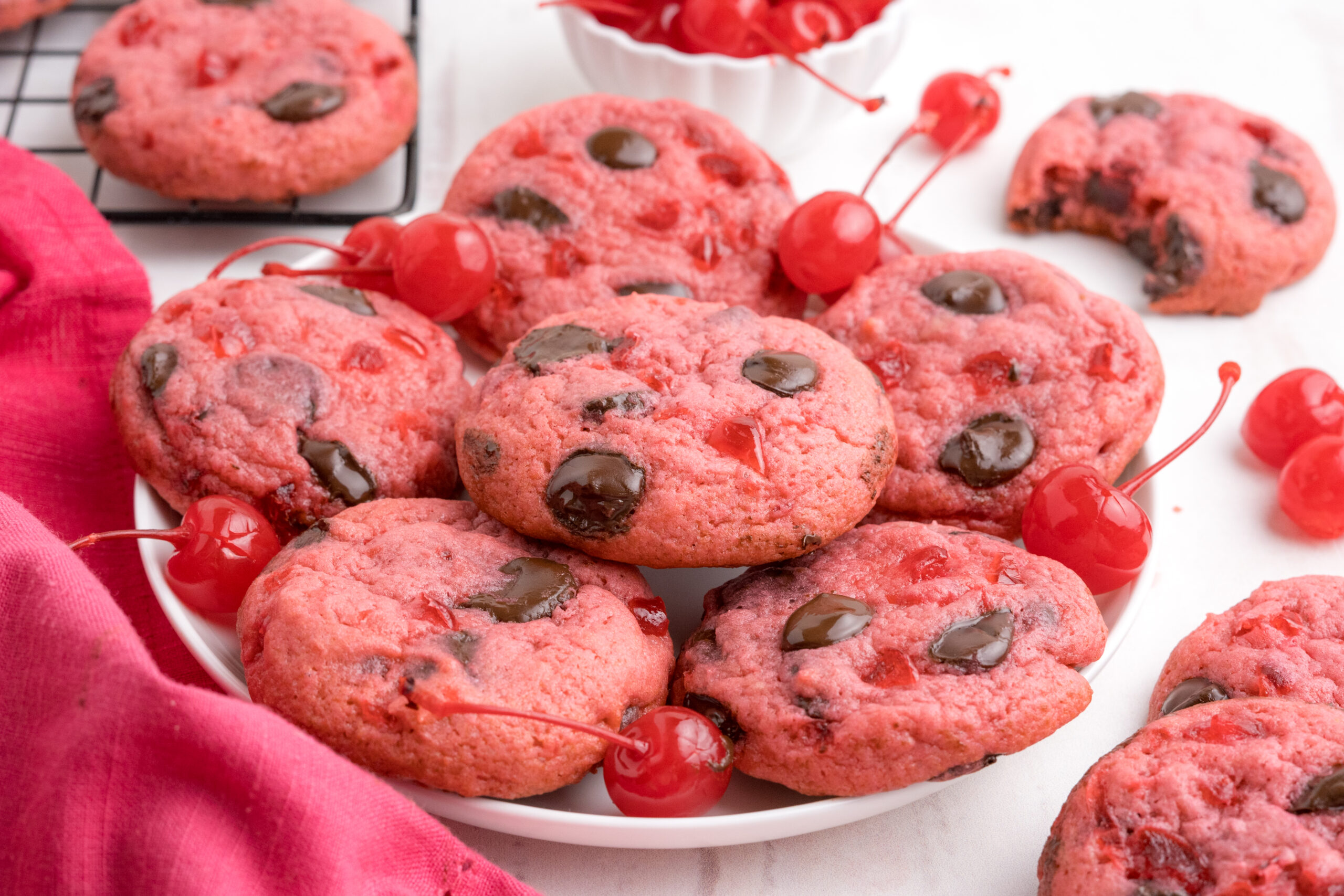 Cherry Chocolate Chip Cookies on a white plate with a few cherries all around them 