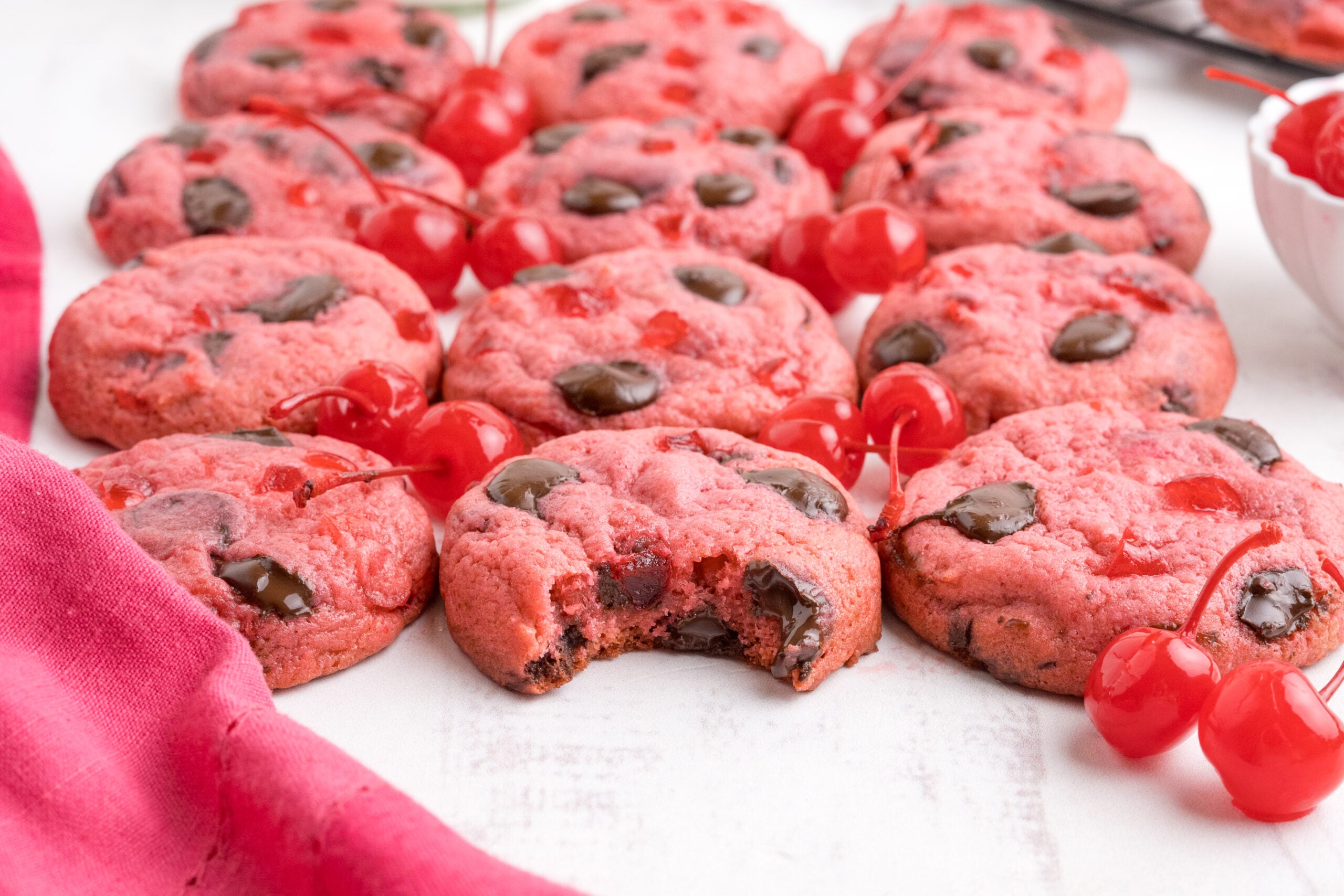 Cherry Chocolate Chip Cookies on a white table with a few cherries in front 