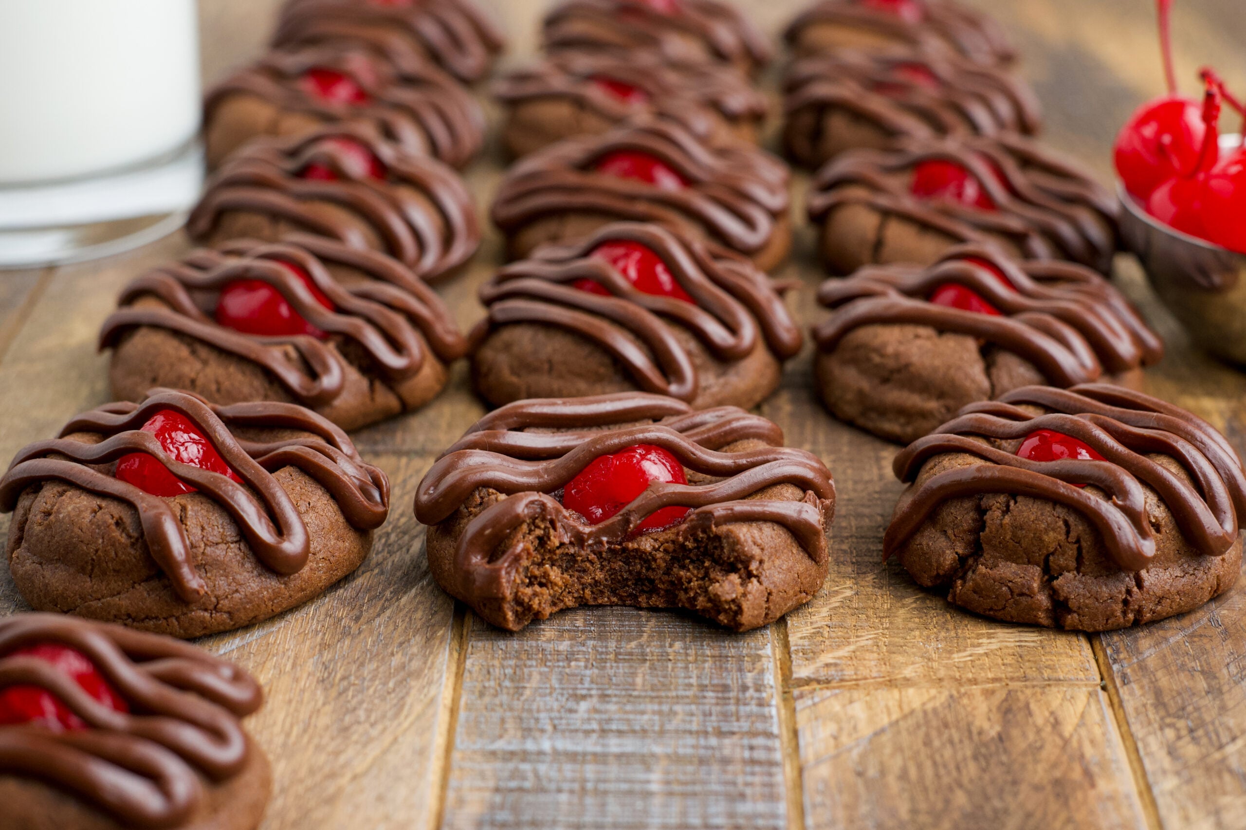 Chocolate Cherry Cookies on a wooden table with the front one missing a bite 