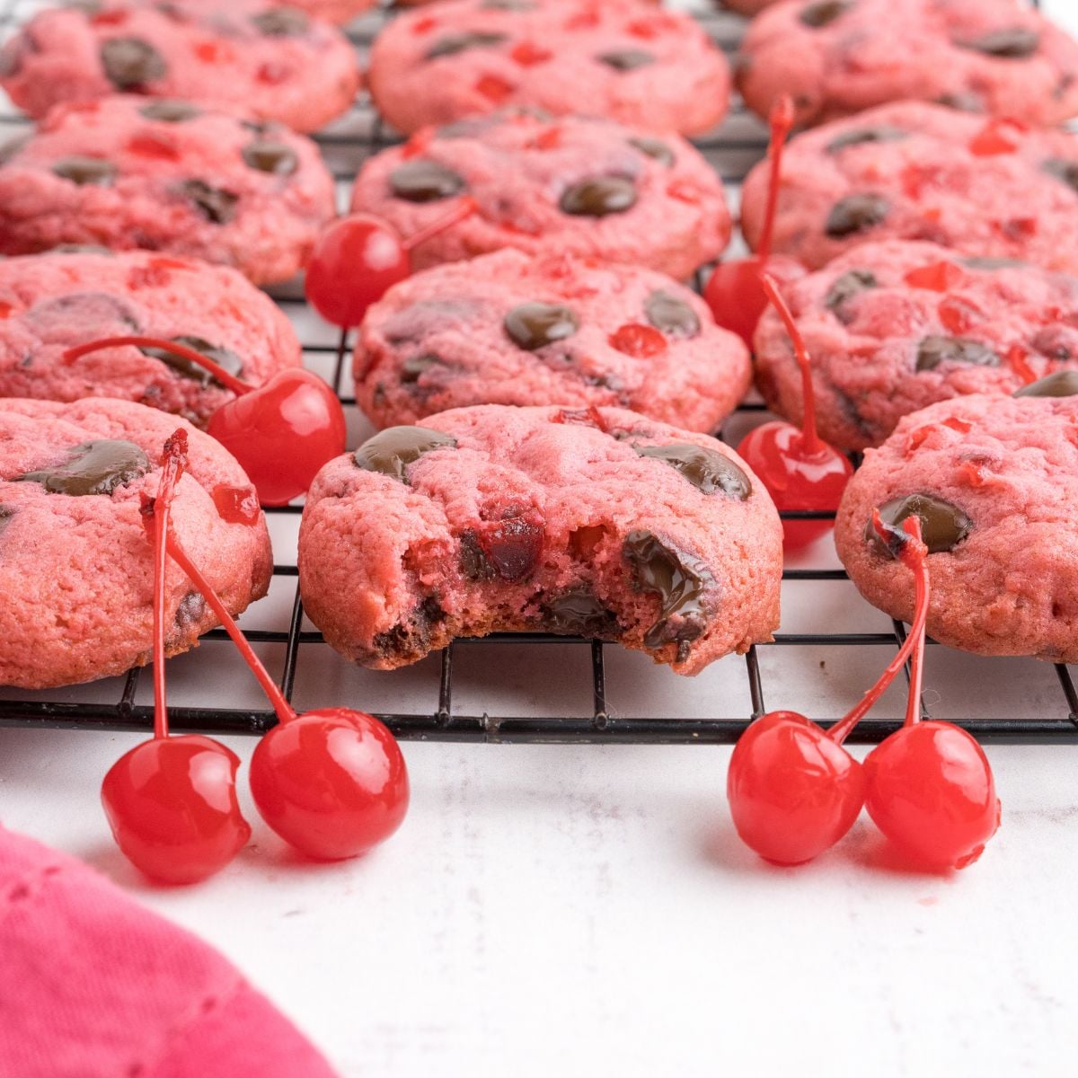 Cherry Chocolate Chip Cookies on a cookie tray with a few cherries on the table in front of the container 