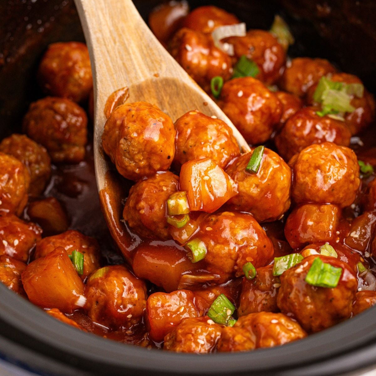 Slow Cooker 3 Ingredient Hawaiian Meatballs in a crockpot with a wooden spoon with some on it 