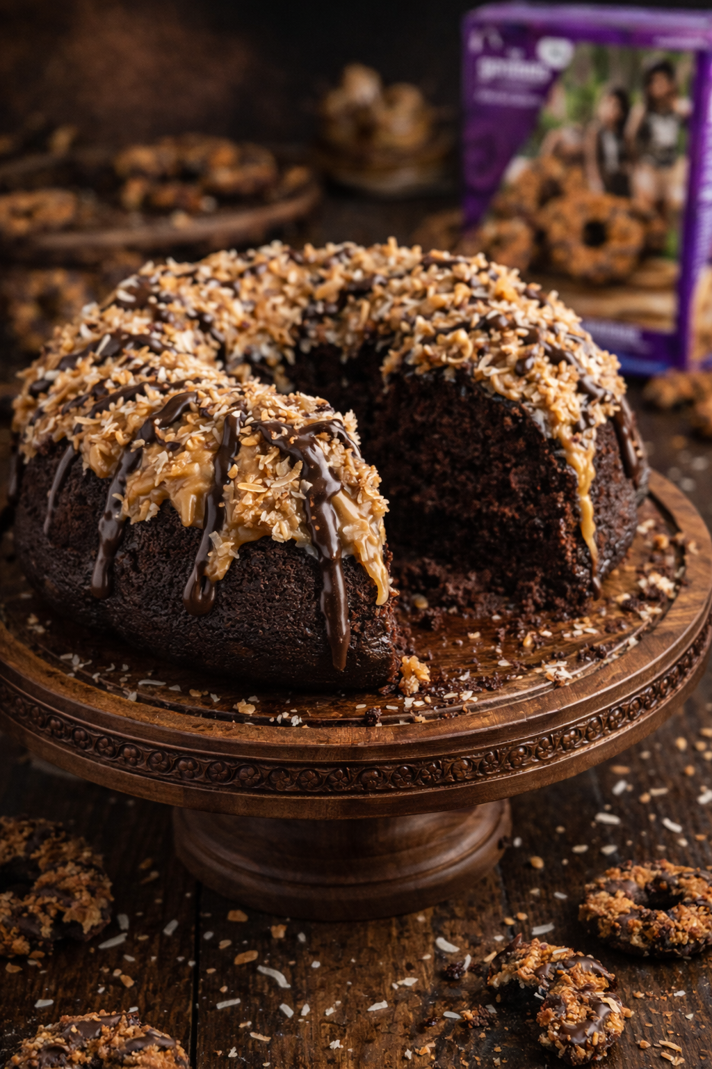 Whole Samoa Cake with a slice missing on a pretty wood cake stand on a dark table