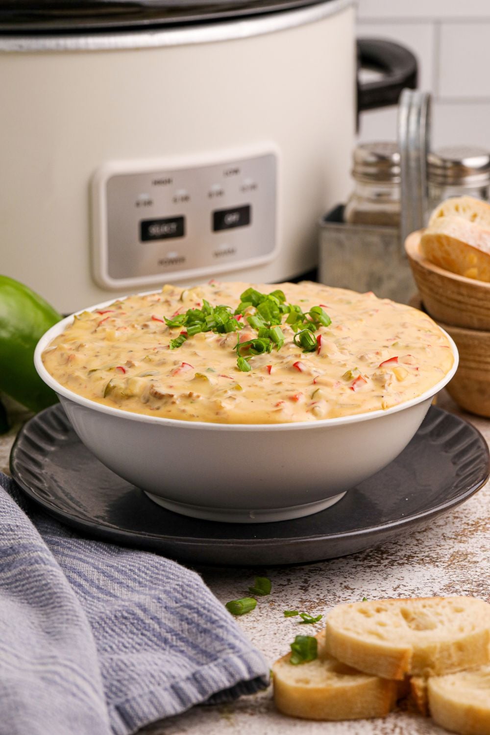 Crock Pot Philly Cheesesteak Dip in a bowl sitting on plate with a slow cooker in the background of the image