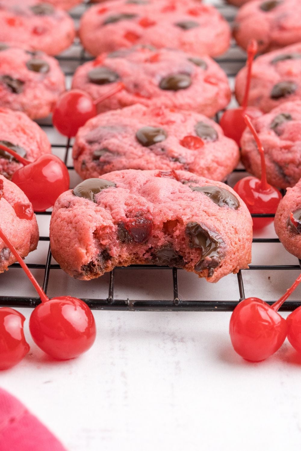 close up of cookies on a metal cooling rack with a few maraschino cherries scattered on the table 
