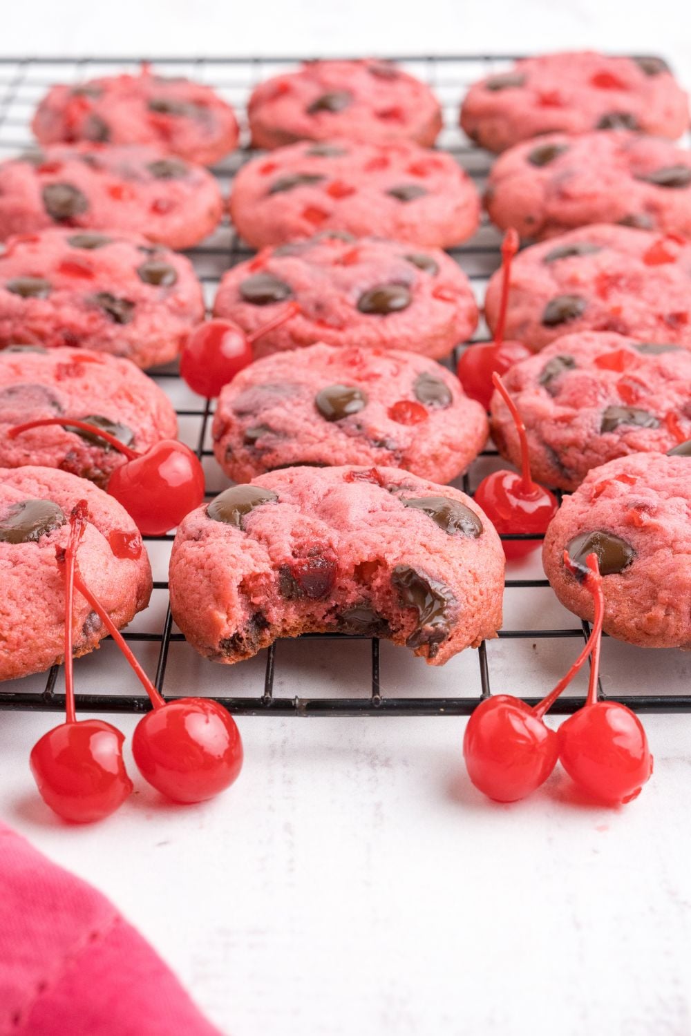 Cherry Chocolate Chip Cookies placed on a cooling rack, with one cookie in the center of tray with a bite taken out of it 