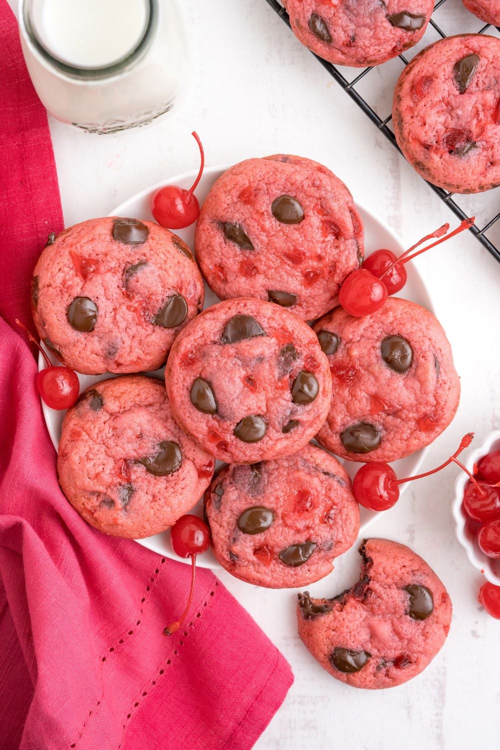 Cherry Chocolate Chip Cookies on a plate with a glass of milk and a bite of cookie taken out of one cookie 