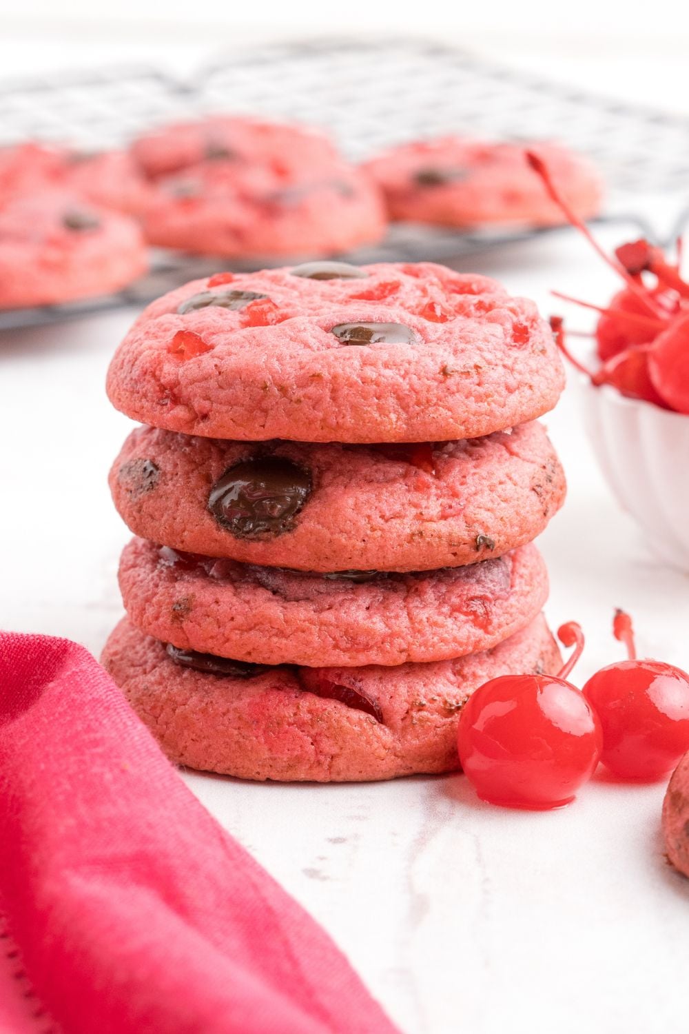 stacked Cherry Chocolate Chip Cookies on the table with two cherries sitting by it 