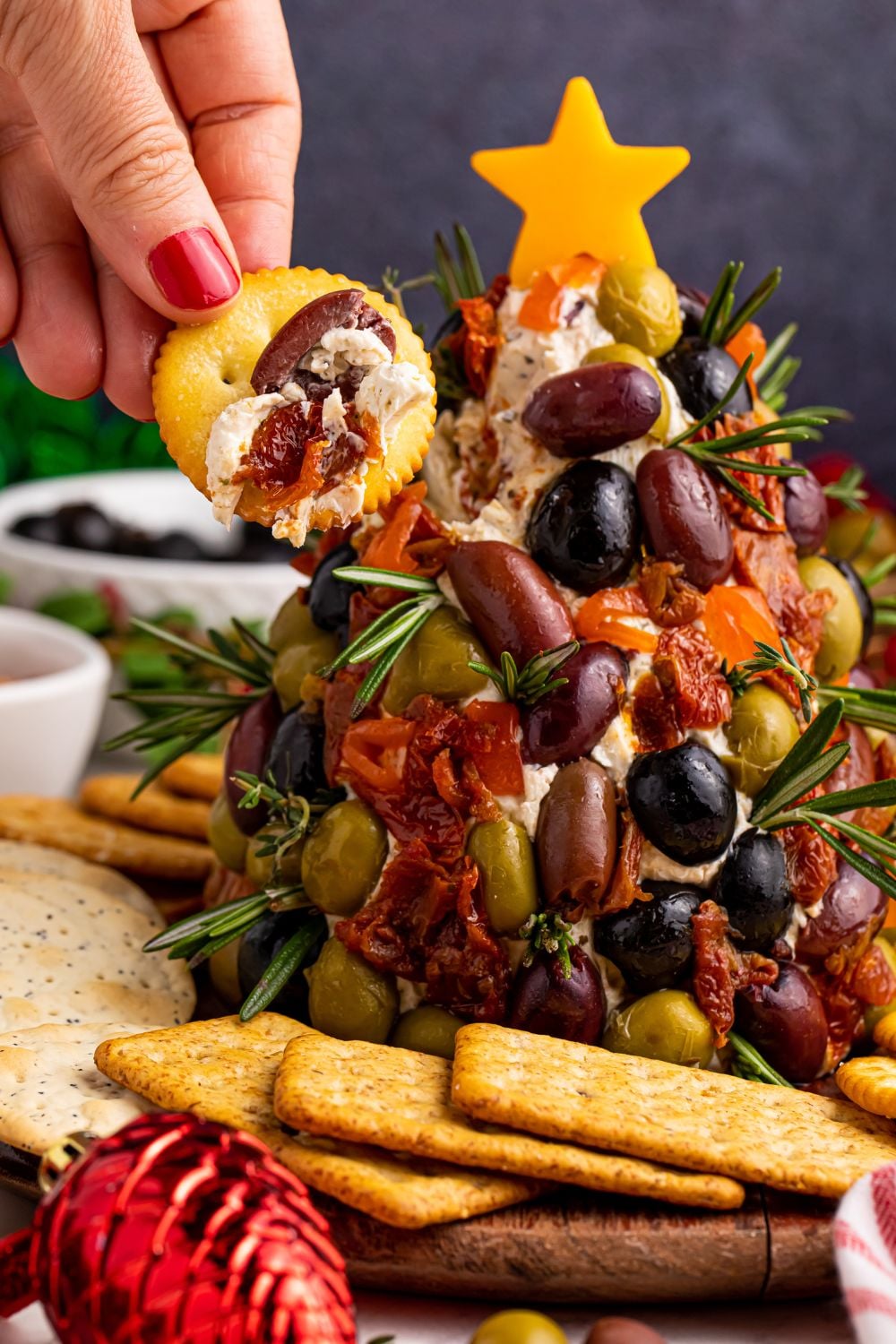 cracker with cream cheese and olive dip on it by the cheeseball on table