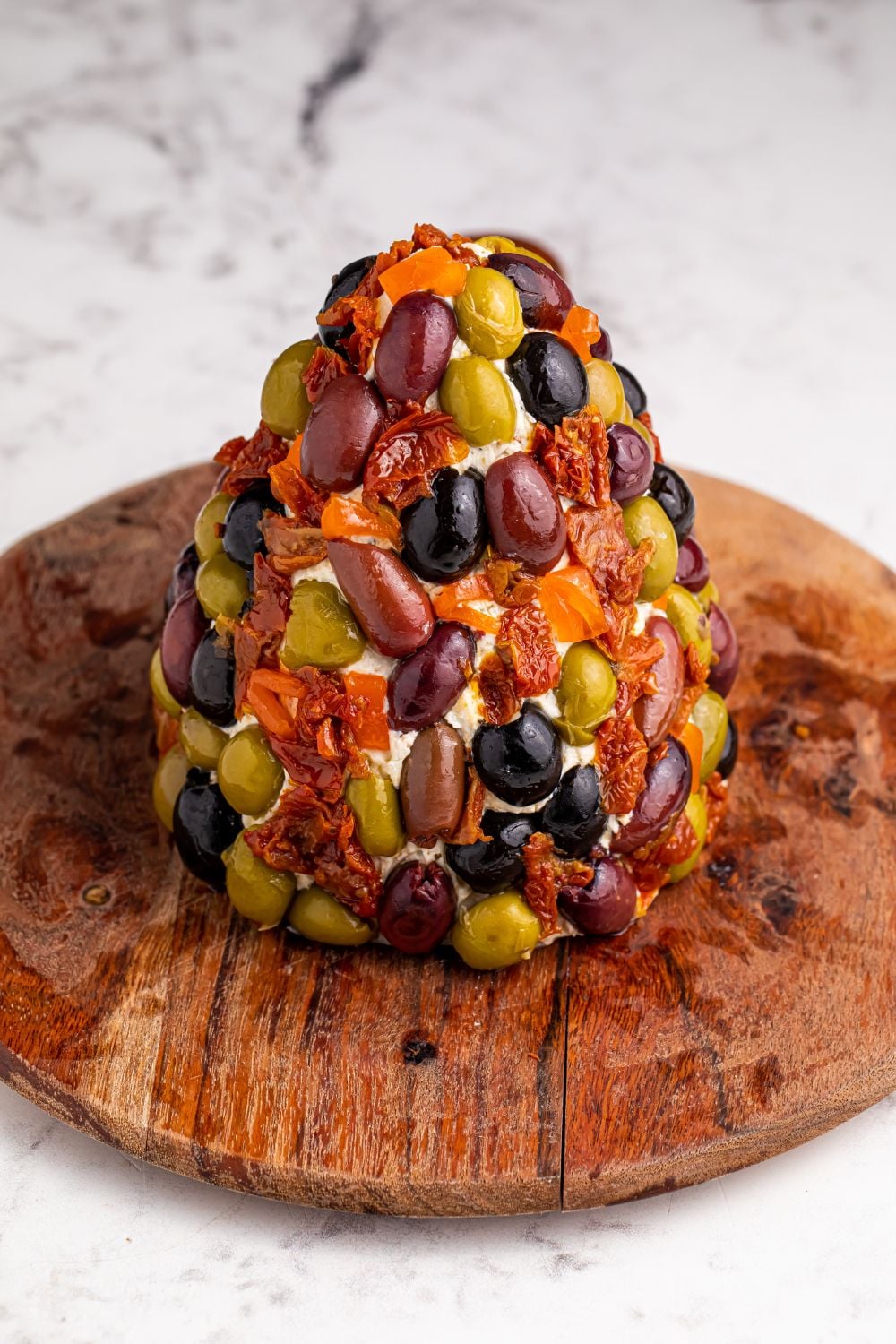 olives and dried tomatoes decorated the outside of a cheeseball