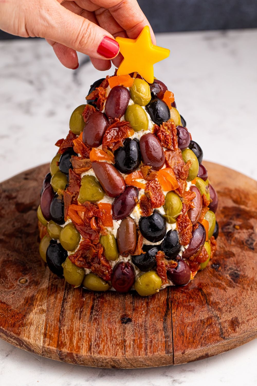 cheeseball decorated with olives and a cheese star being placed on top