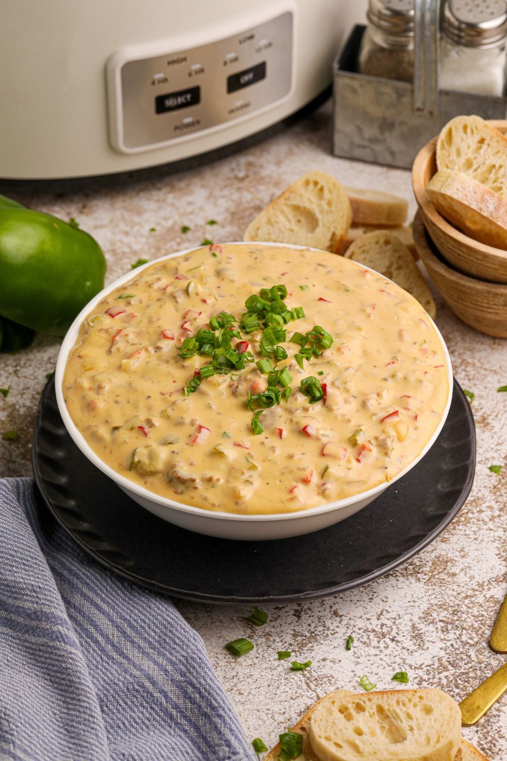Crock Pot Philly Cheesesteak Dip in a white bowl on table with peppers around it on counter and bread slices