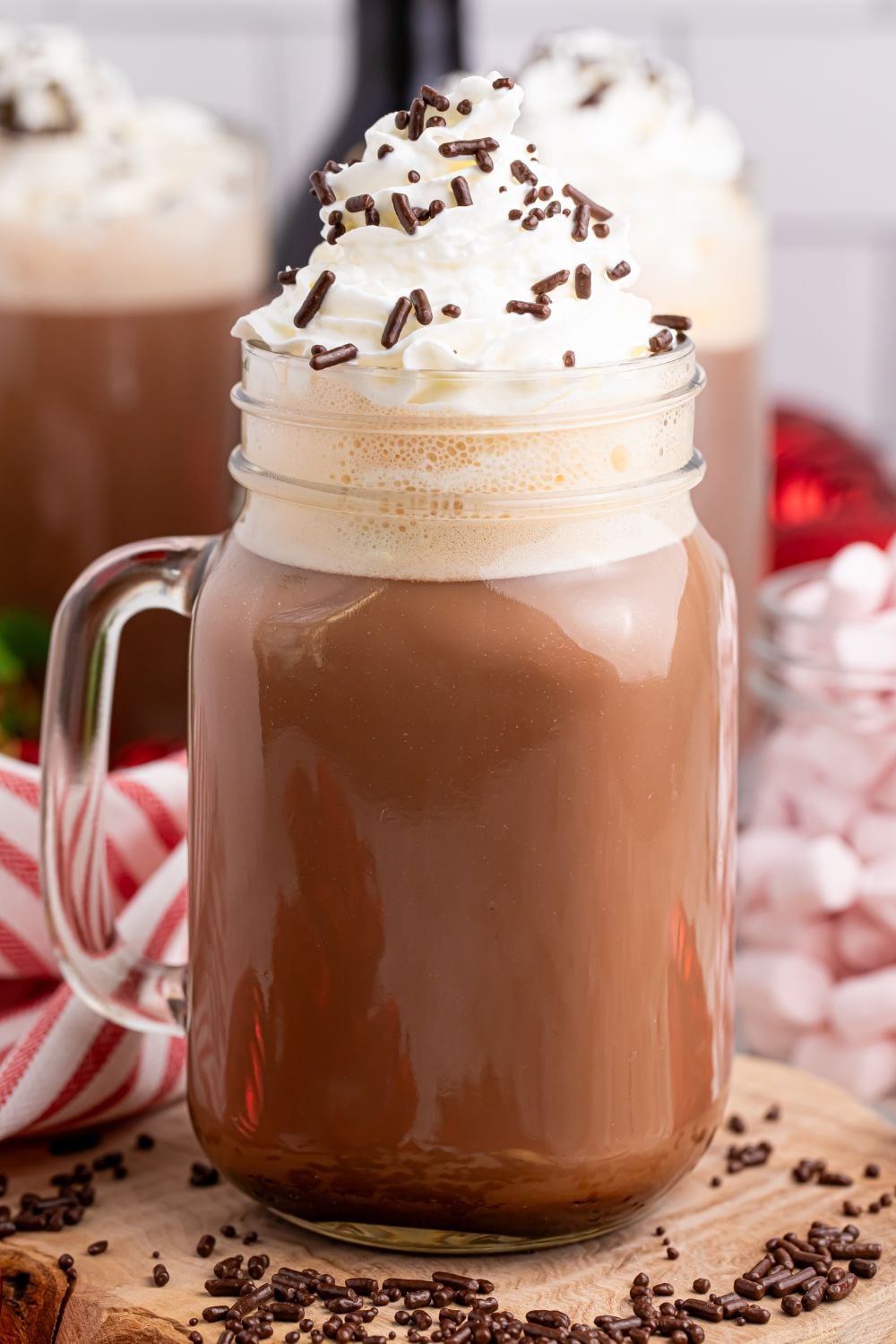 hot chocolate drink on table with whipped cream and sprinkles and then sprinkles around the glass on table