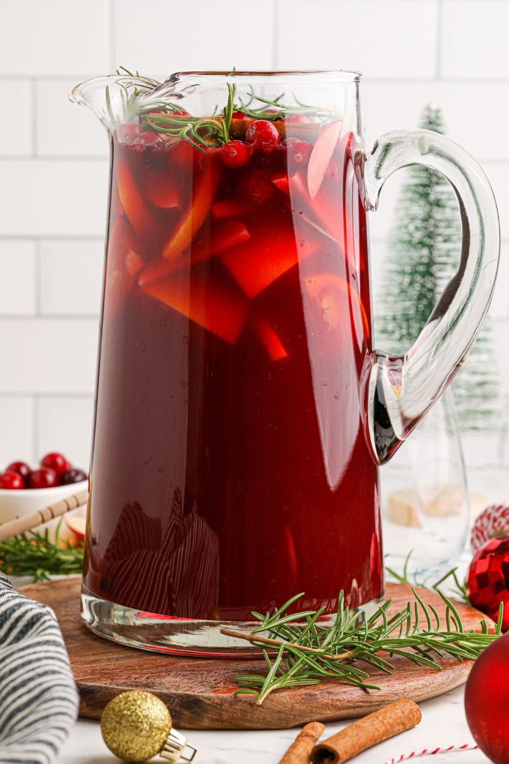 Cranberry Apple Christmas Sangria in a glass pitcher on table with garnishes around it