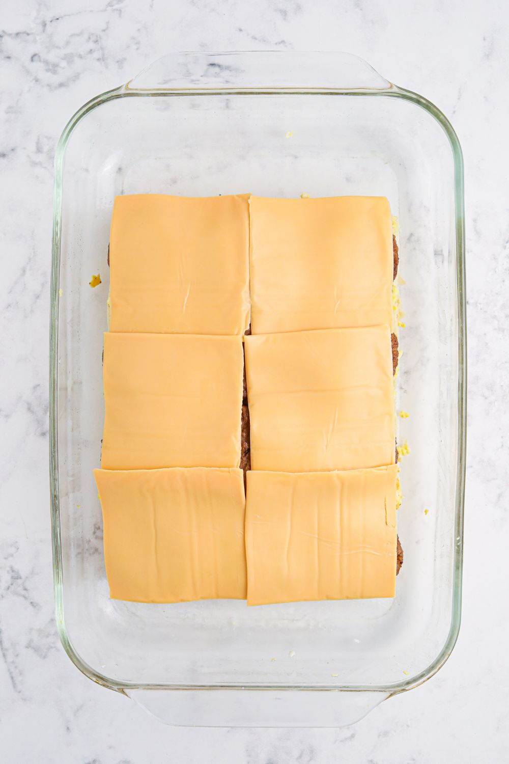 Breakfast Sliders being prepared with cheese on top of sasuasge patties in a 9x13 pan 