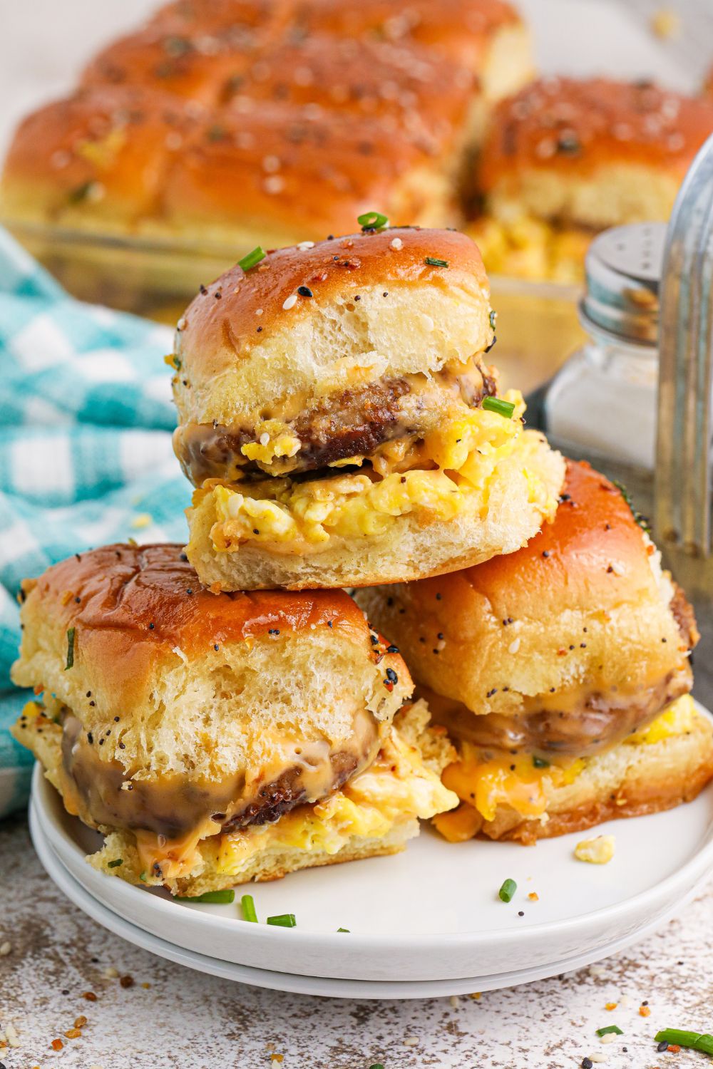 Breakfast Sliders stacked on a plate with a pan of the rest of sliders in the background 