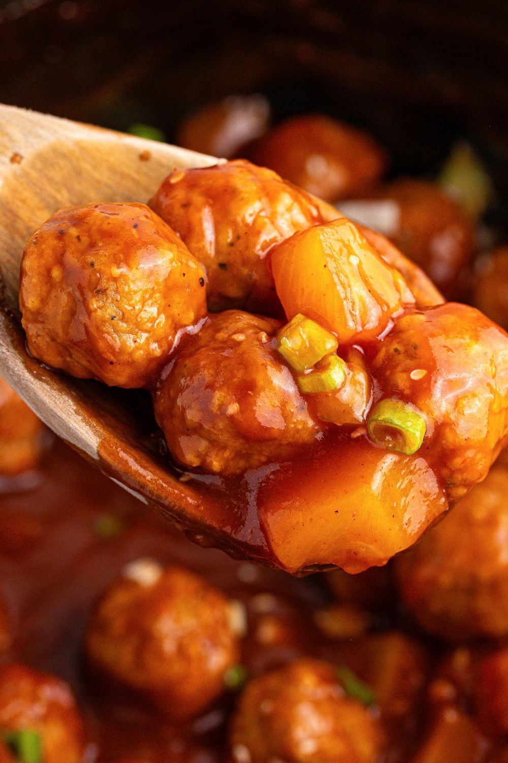 close up of Slow Cooker 3 Ingredient Hawaiian Meatballs on a wooden spoon inside the crockpot 