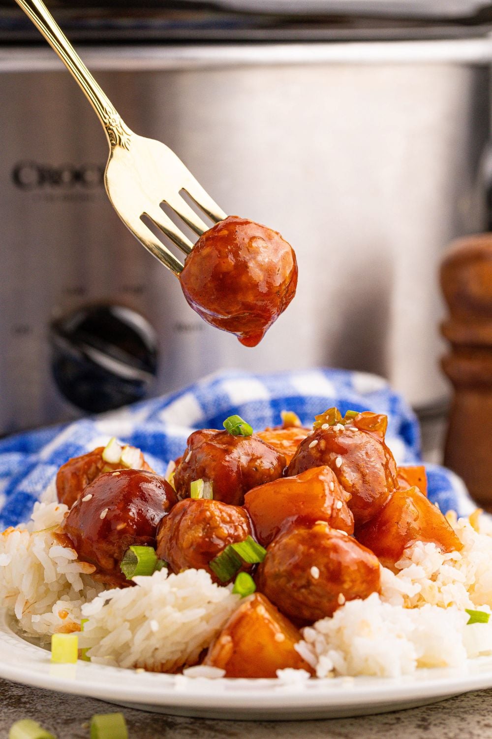 Slow Cooker 3 Ingredient Hawaiian Meatballs on a plate with rice and one poked on a fork above plate 