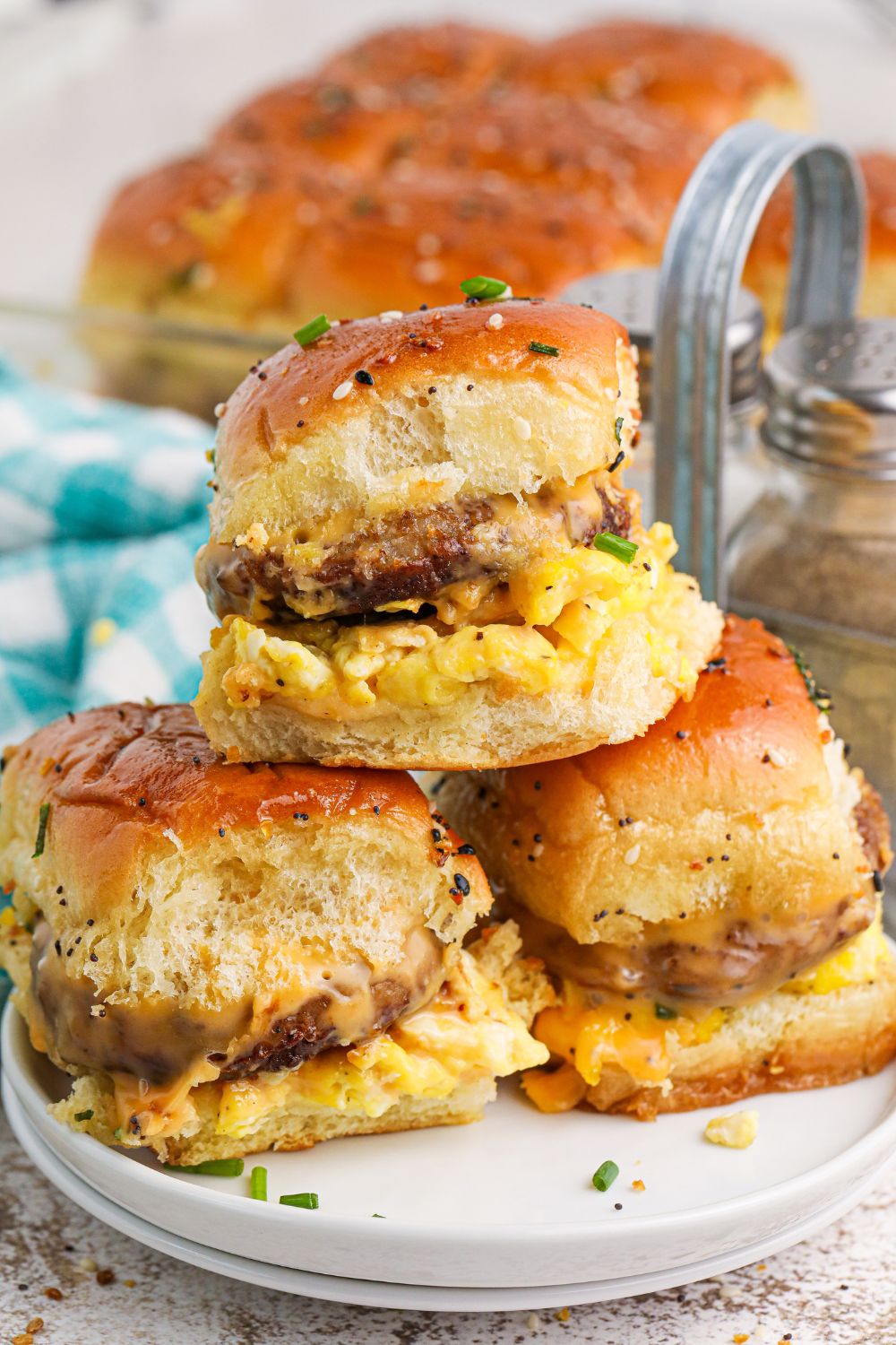 Breakfast Sliders stacked on a plate with a pan of sliders behind it on table 
