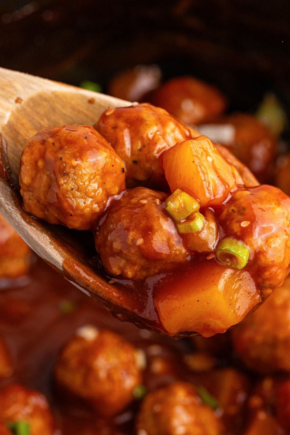 Slow Cooker 3 Ingredient Hawaiian Meatballs on a wooden spoon in a slow cooker 
