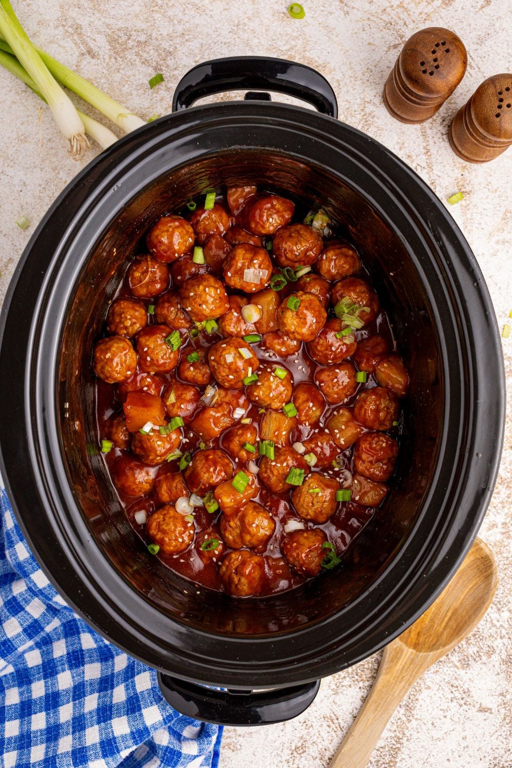 Slow Cooker 3 Ingredient Hawaiian Meatballs in a slow cooker sitting on table with spoon and other items around the slow cooker 