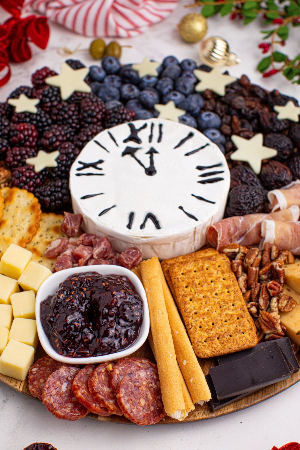 New Year's Eve Charcuterie Board that is on a table with some Christmas decor around the round charcuterie board 