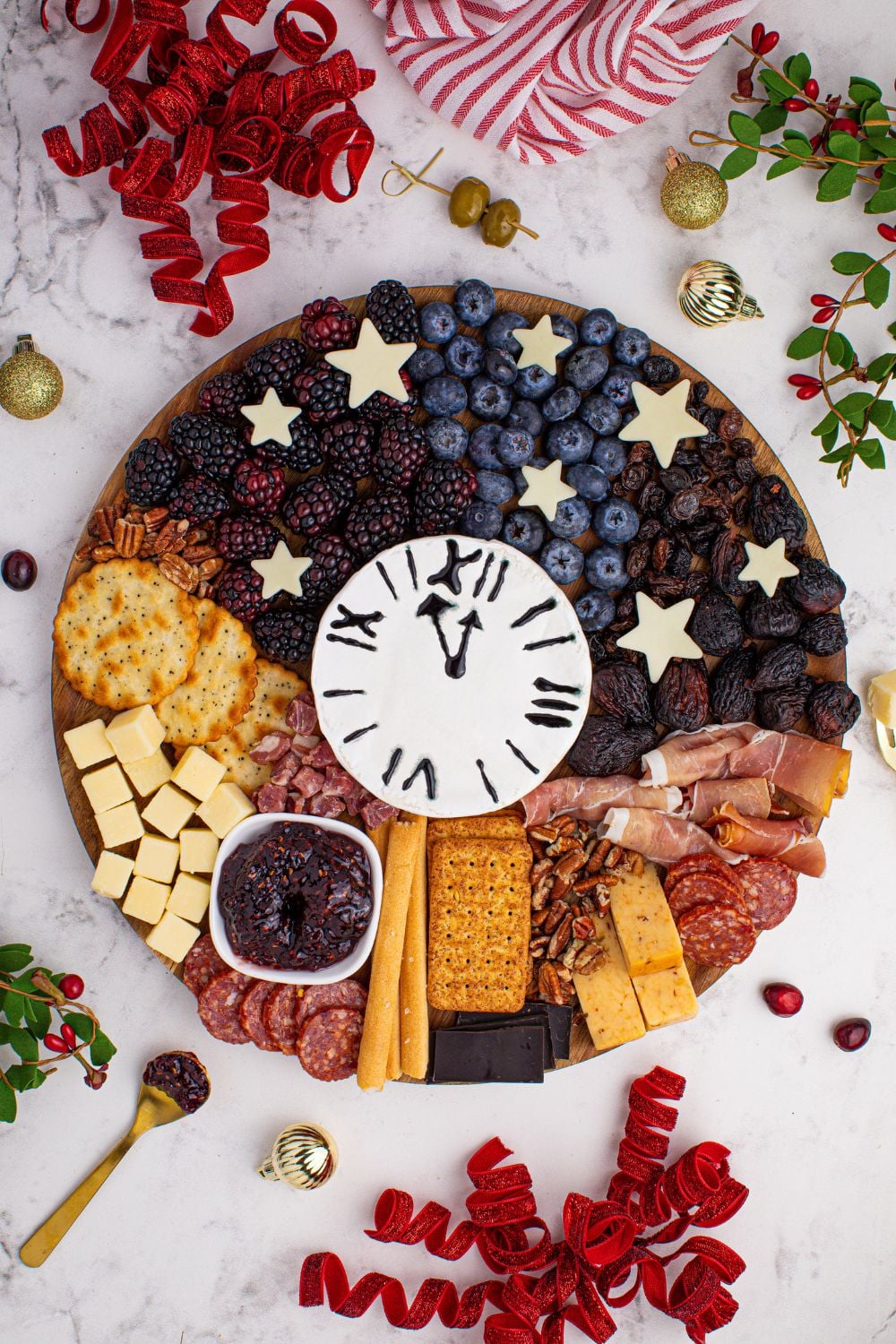 New Year's Eve Charcuterie Board on table with ribbon, berries and herbs around the table 