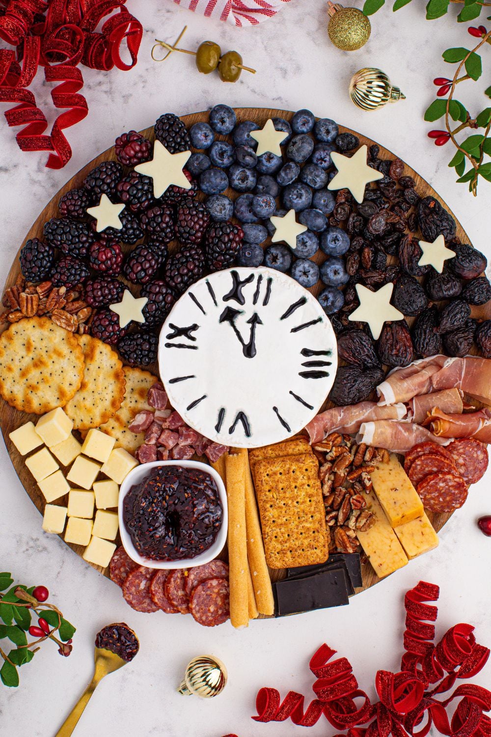 New Year's Eve Charcuterie Board sitting on table with CHristmas decor around it and some fruits on table 