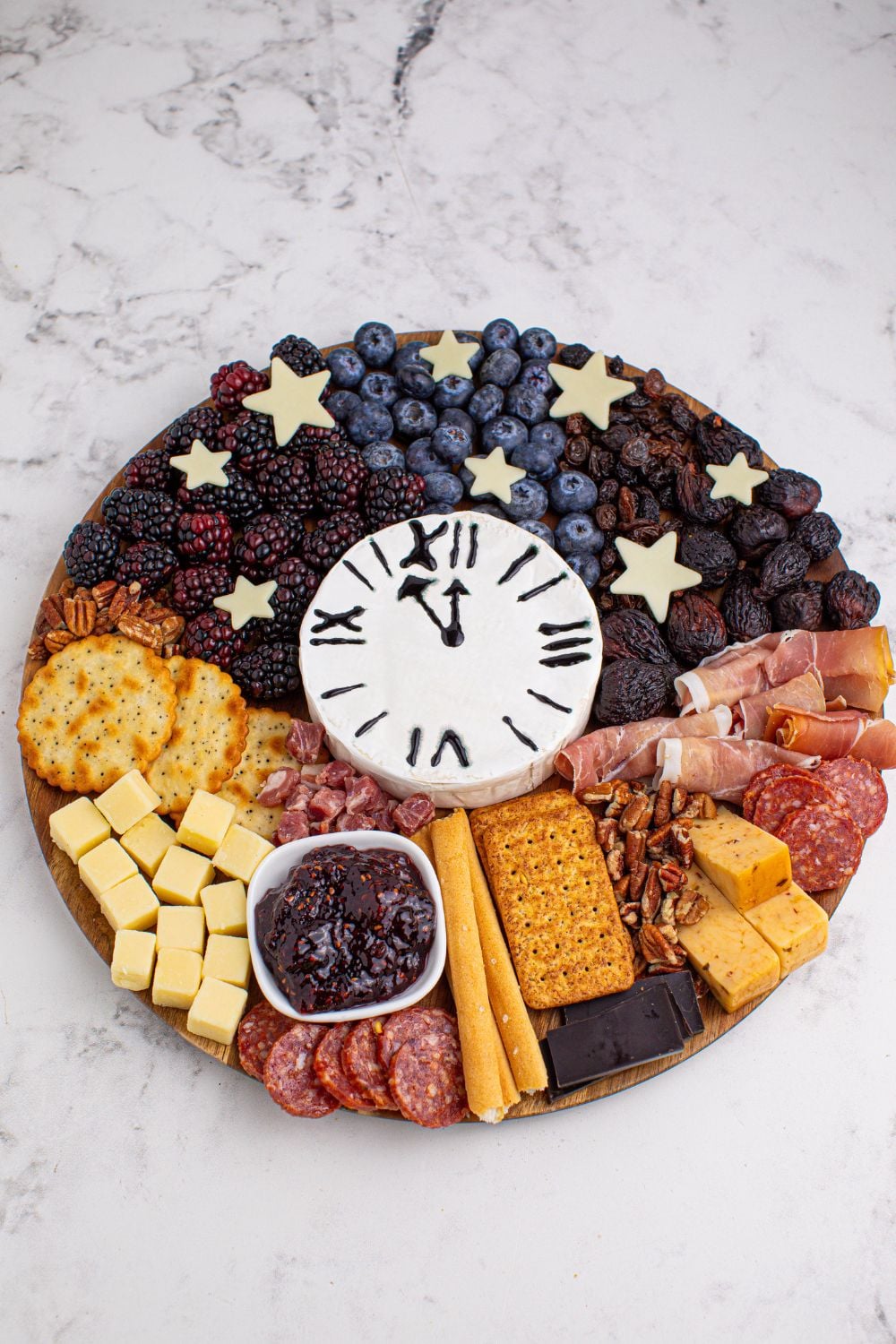 New Year's Eve Charcuterie Board on a marble table showcasing all the snacking items on the board with a brie bock in center that looks like a clock 