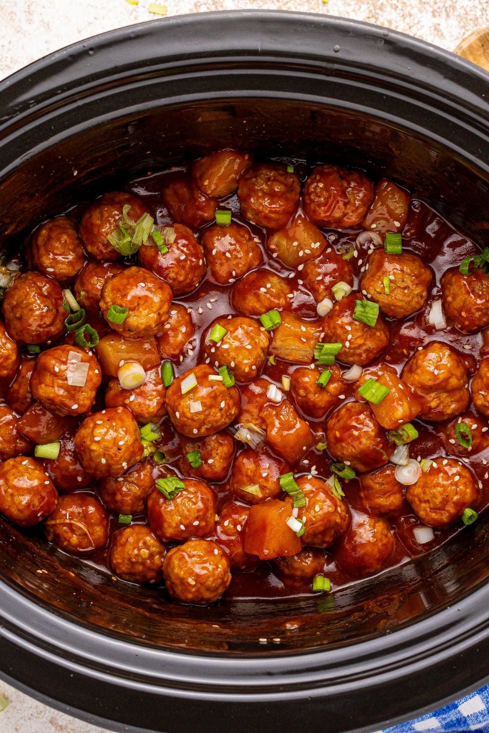 Slow Cooker 3 Ingredient Hawaiian Meatballs in a slow cooker on the table with garnishes on top 