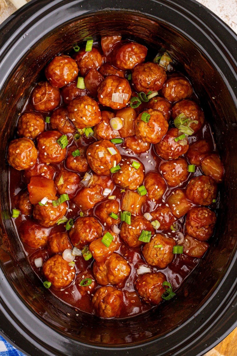 cooked Slow Cooker 3 Ingredient Hawaiian Meatballs with green onions garnished on top of the slow cooker pan