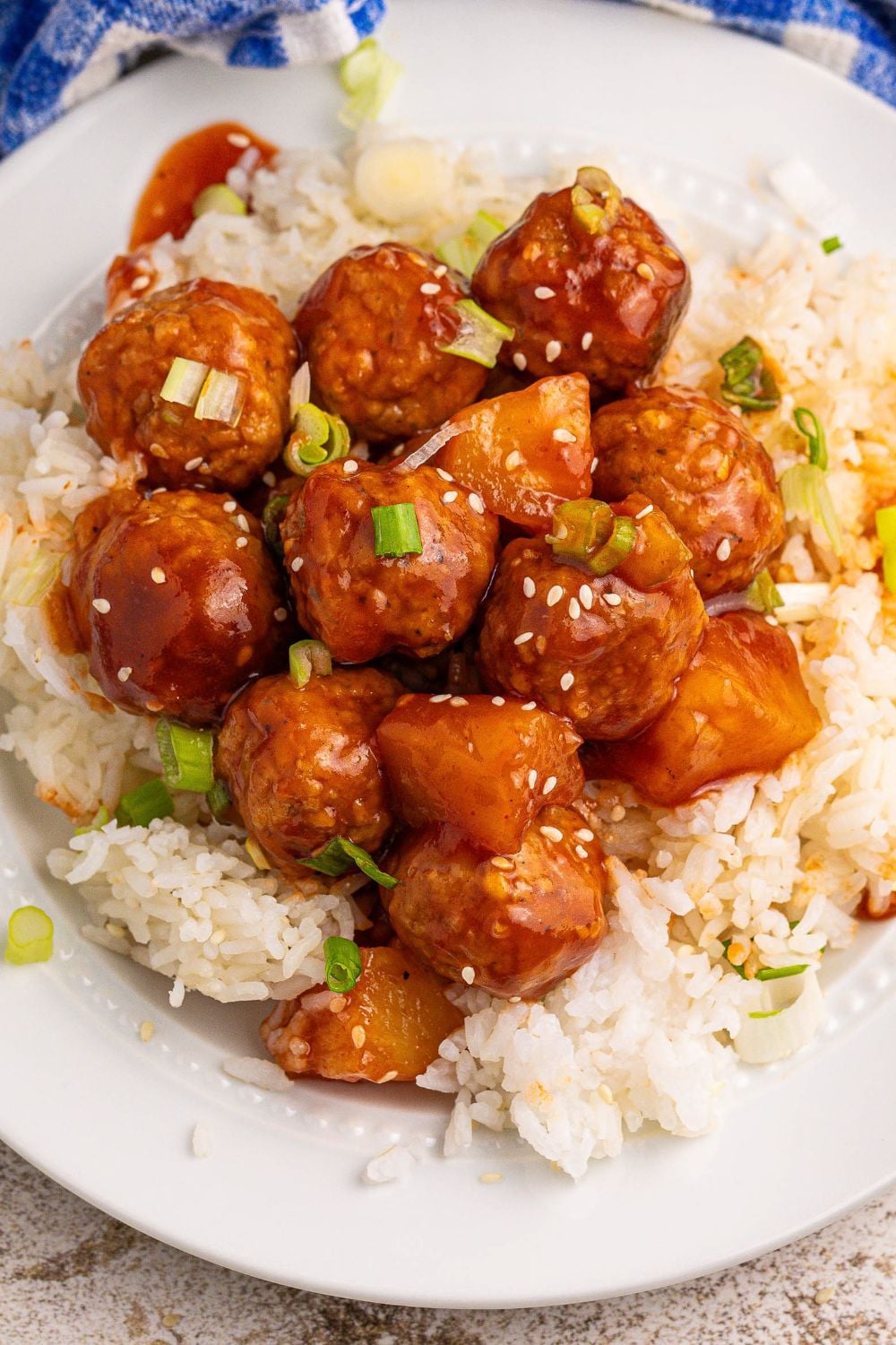 Slow Cooker 3 Ingredient Hawaiian Meatballs on a plate with a bed of rice under it and sesame garnish 