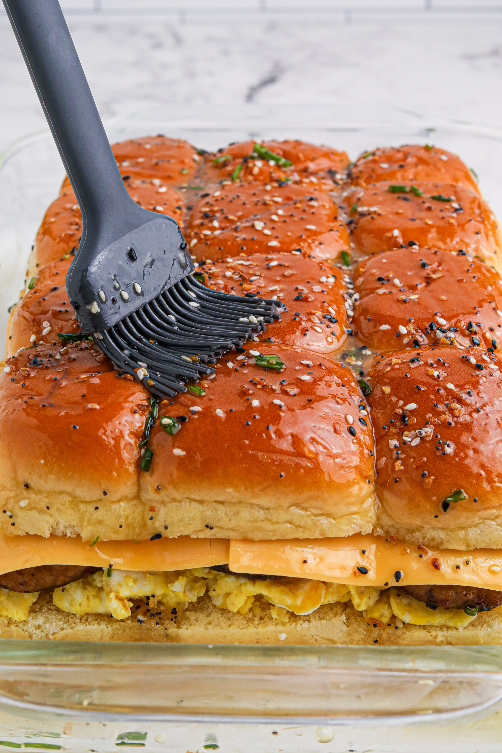Breakfast Sliders uncut in a baking dish with batter being brushed on top