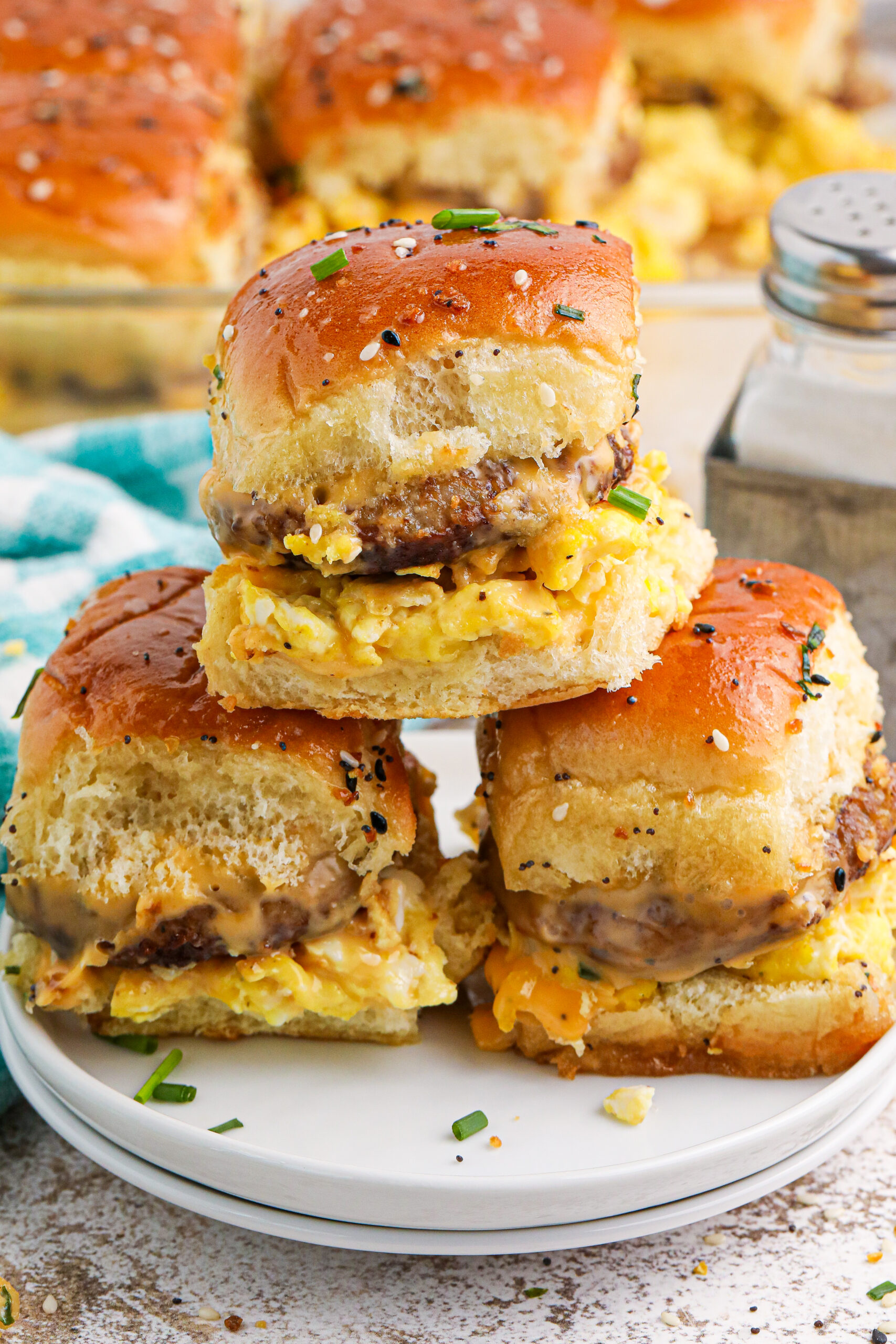 Breakfast Sliders on a plate with some fresh herbs sprinkled on table in the front 