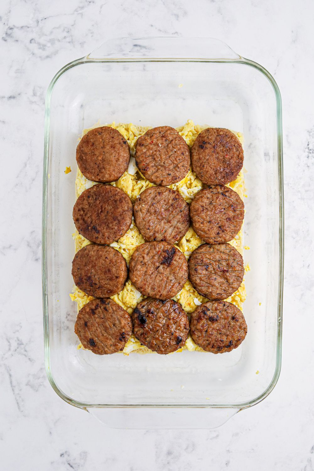 Breakfast Sliders being prepared with eggs and sausage patties on top of the bottom buns 