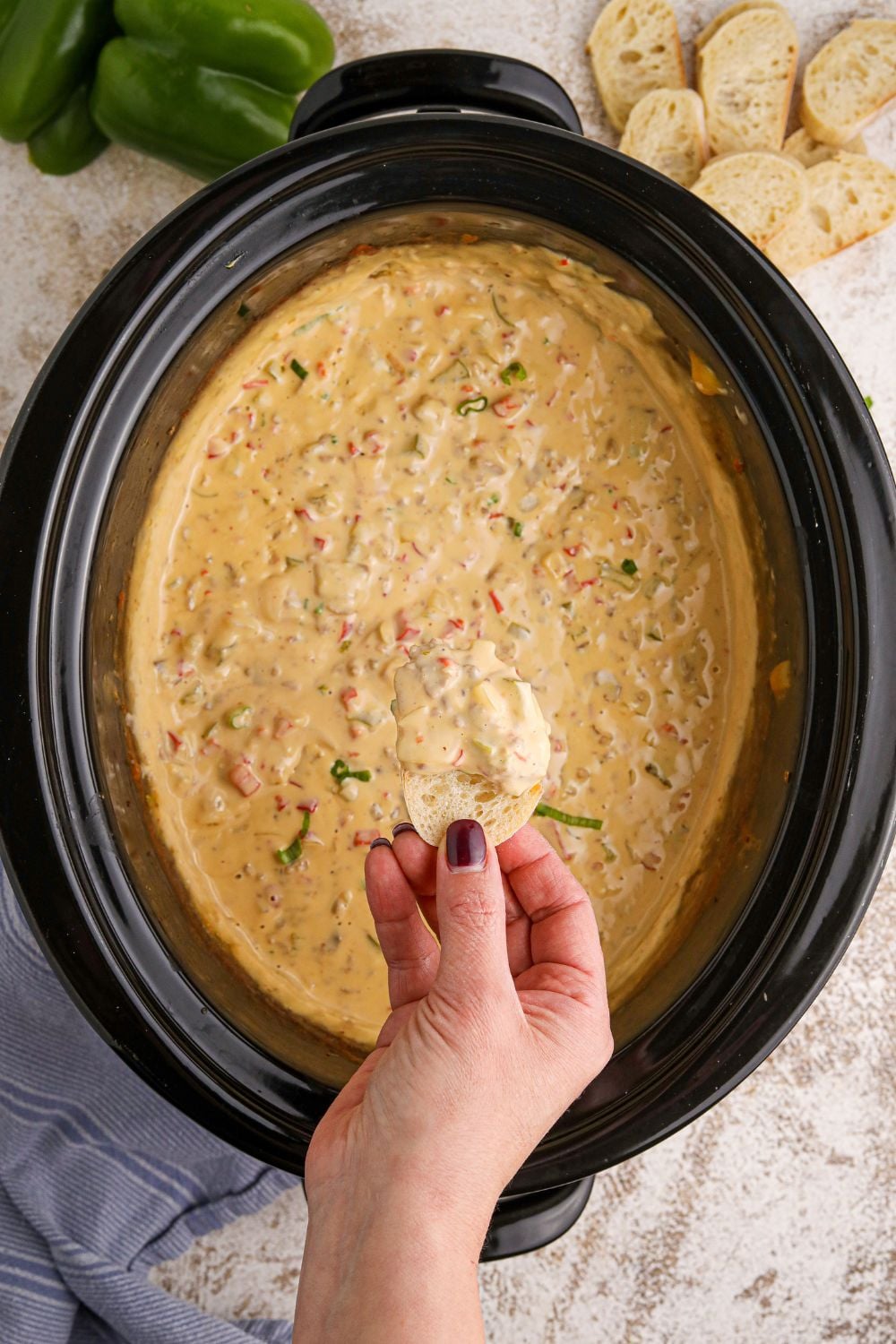 Crock Pot Philly Cheesesteak Dip with a hand and a piece of bread dipped in the creamy dip above the crockpot