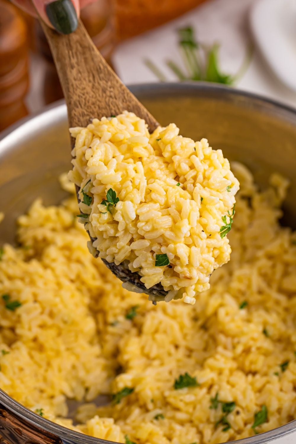 Souper Rice in a pan on table with a wooden spoon with some rice on the spoon being held above the pan